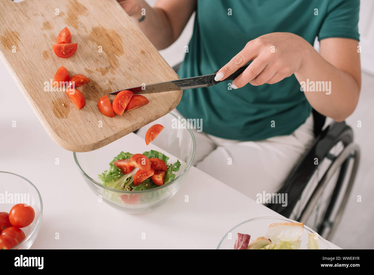 Vue partielle de la femme handicapée ajoutant des tranches de tomate dans bol en verre dans la cuisine Banque D'Images