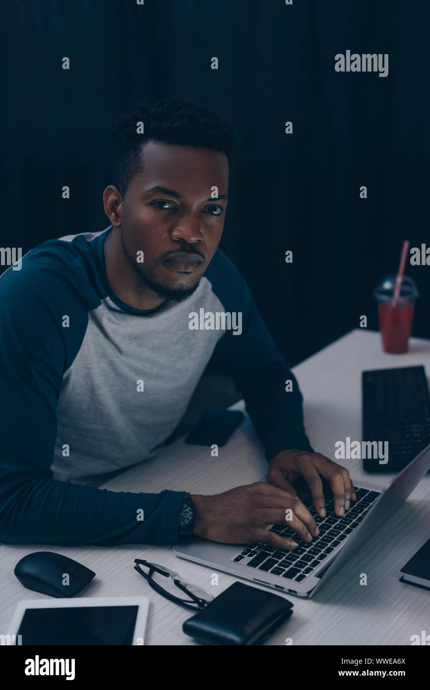 African American programmer looking at camera tout en travaillant de nuit in office Banque D'Images