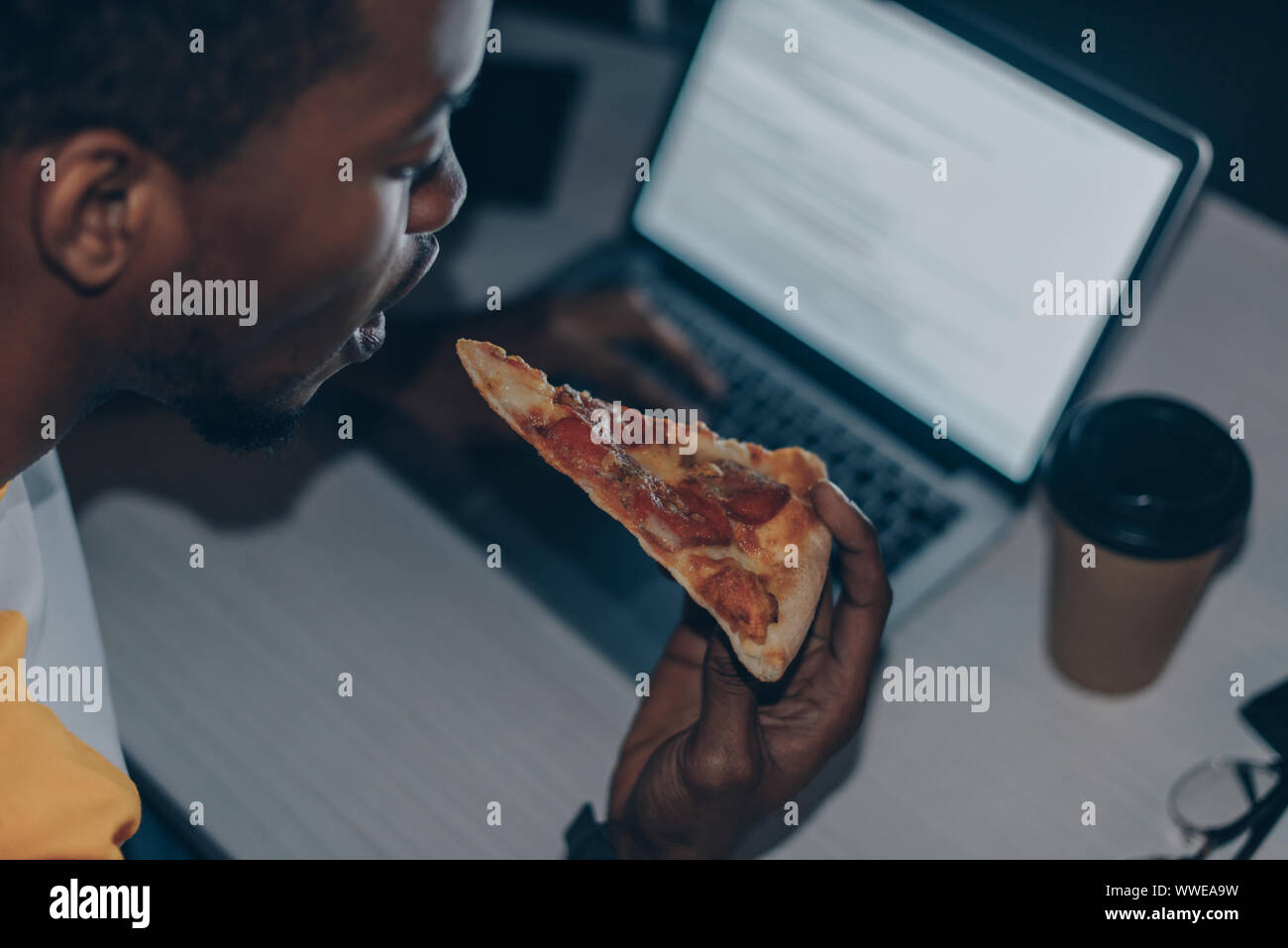 Young african american programmer eating pizza tout en travaillant de nuit in office Banque D'Images