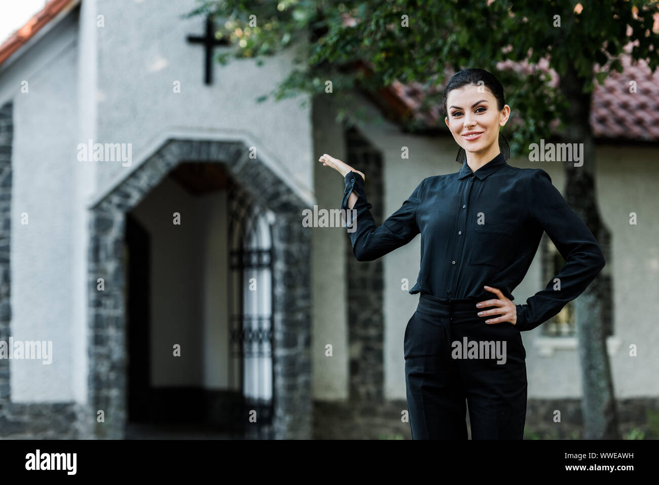 Cheerful woman standing with hand on hip tout en gesticulant près de l'église Banque D'Images