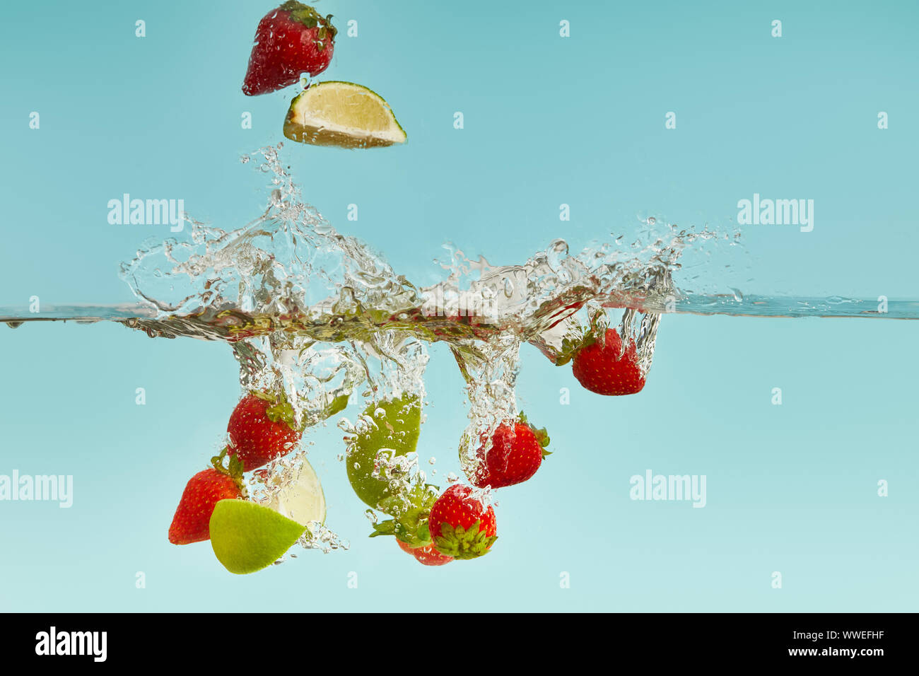 Morceaux de lime et les fraises de tomber dans l'eau avec des vagues sur fond bleu Banque D'Images
