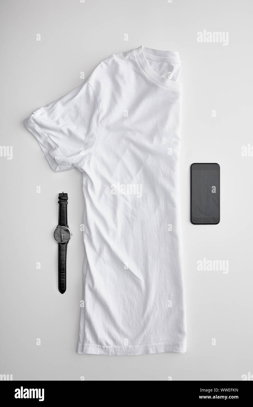 Mise à plat avec l'échantillon à blanc plié en deux t-shirt près de montres et smartphone sur fond blanc Banque D'Images