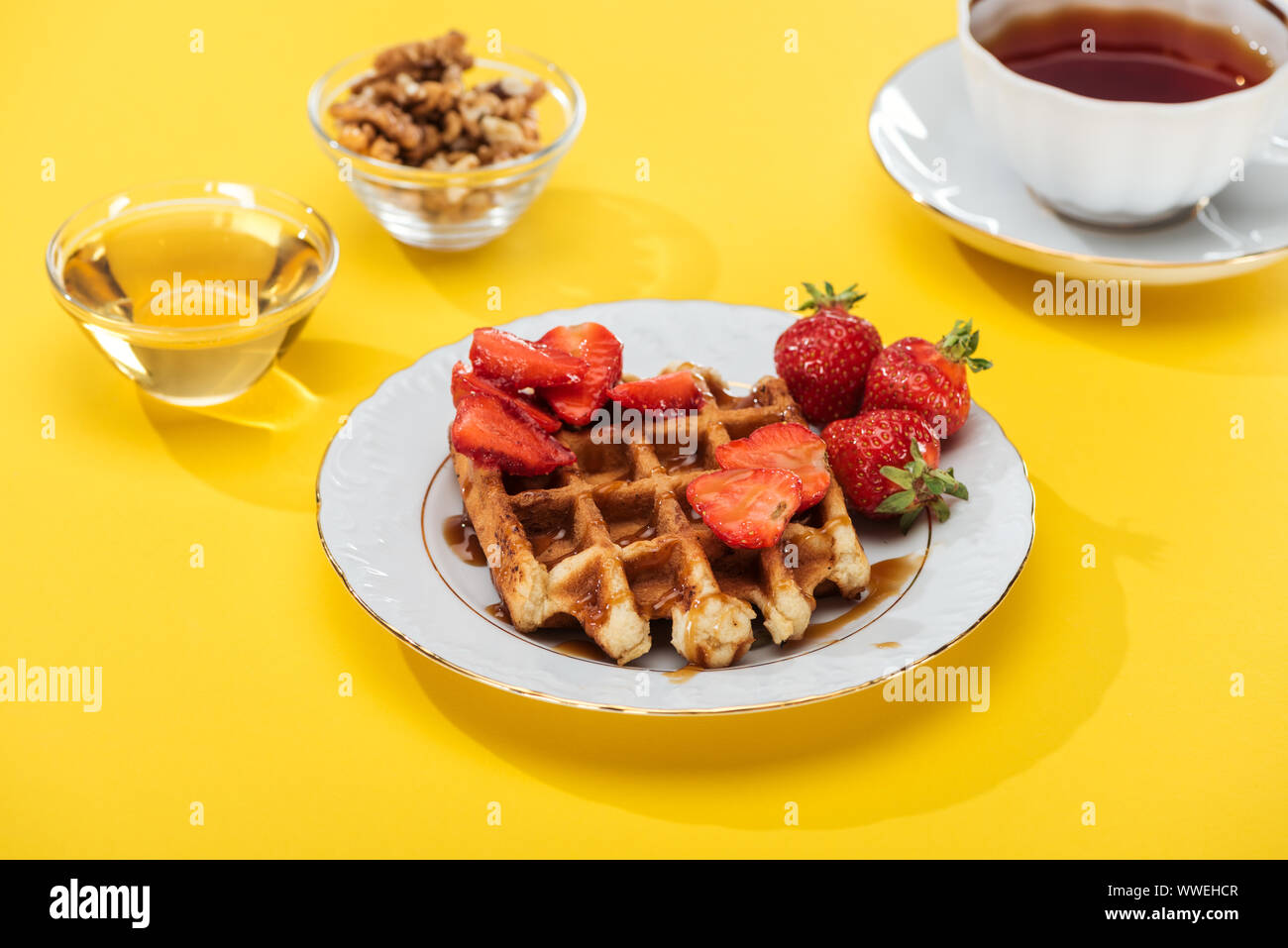 Petit-déjeuner servi avec waffle et fraises à plaqué, miel, noix et d'un plateau sur fond jaune Banque D'Images