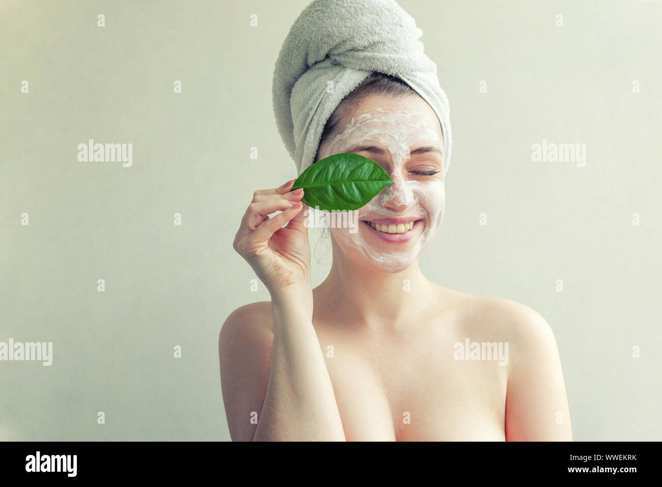 Portrait of woman in towel on head avec blanc masque nourrissant ou la crème sur le visage et le vert feuille dans la main, fond blanc isolé. Nettoyage de la peau cosmétiques bio eco spa concept Banque D'Images