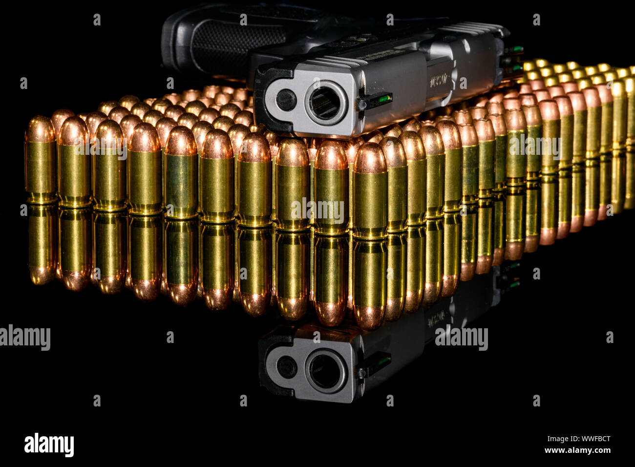 Pistolet semi-automatique sur les rangées de munitions, de munitions sur fond noir et de réflexion Banque D'Images