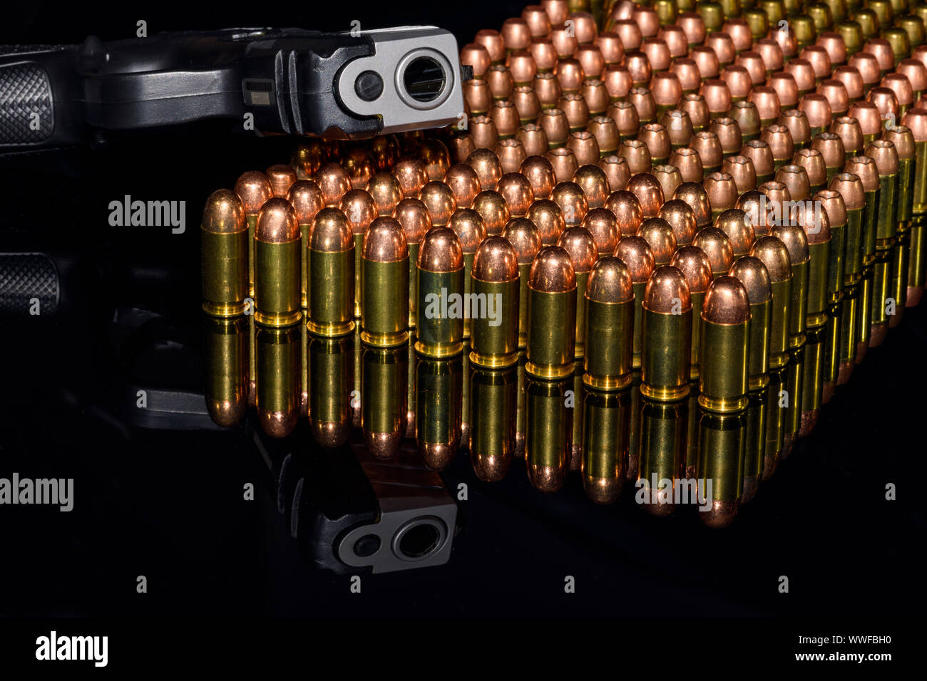 Pistolet semi-automatique sur les rangées de munitions, de munitions sur fond noir et de réflexion Banque D'Images