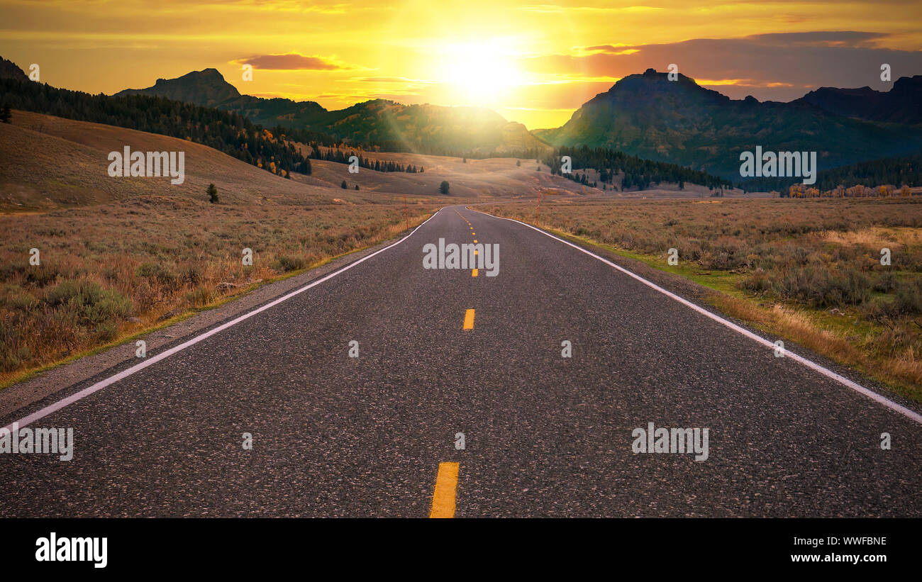 La route à deux voies en direction de la lumière orangée de l'aube sur un col de montagne à l'horizon. Pour la liberté conceptuelle, d'un nouveau jour, et de nouvelles possibilités. Banque D'Images