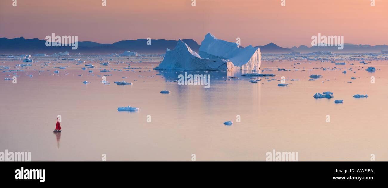 Croisière voilier rouge parmi des icebergs dans la baie de Disko glacier durant la saison de soleil de minuit de l'été polaire. Ilulissat, Groenland. L'Unesco Banque D'Images