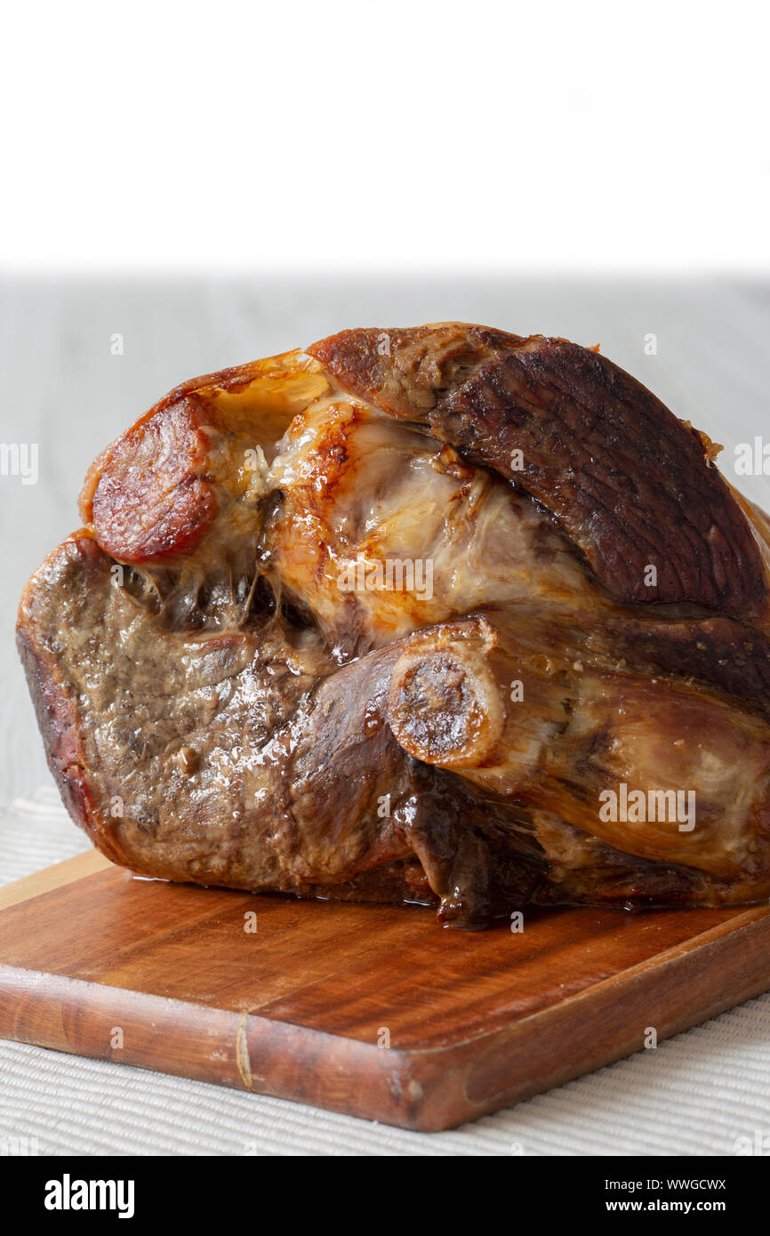 Gigot d'agneau rôti en appui sur une planche à découper en bois et set de table. Fond en bois gris Banque D'Images