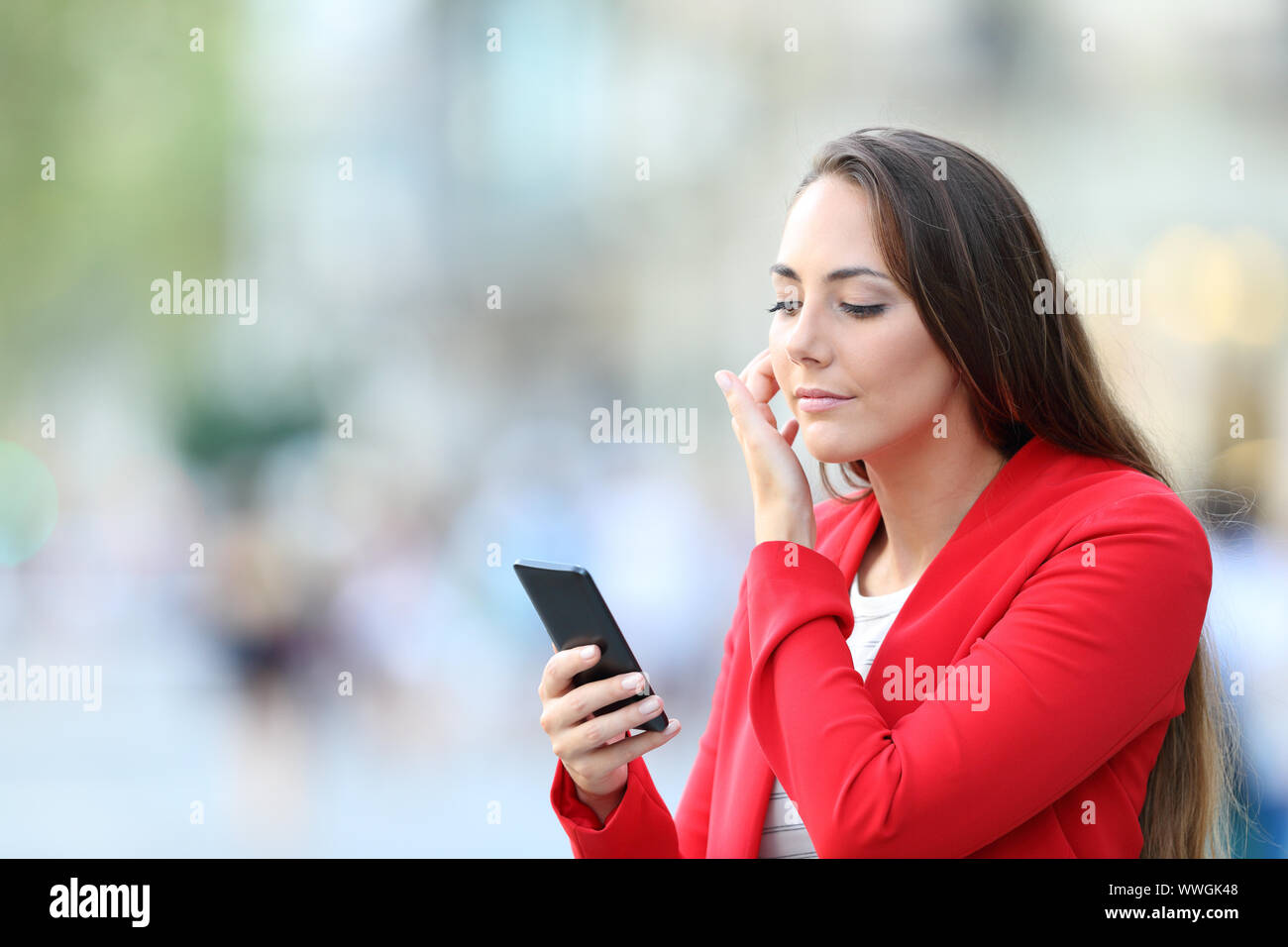 Fashion femme en rouge à l'aide de smart phone comme un miroir de peigner ses cheveux dans la rue Banque D'Images