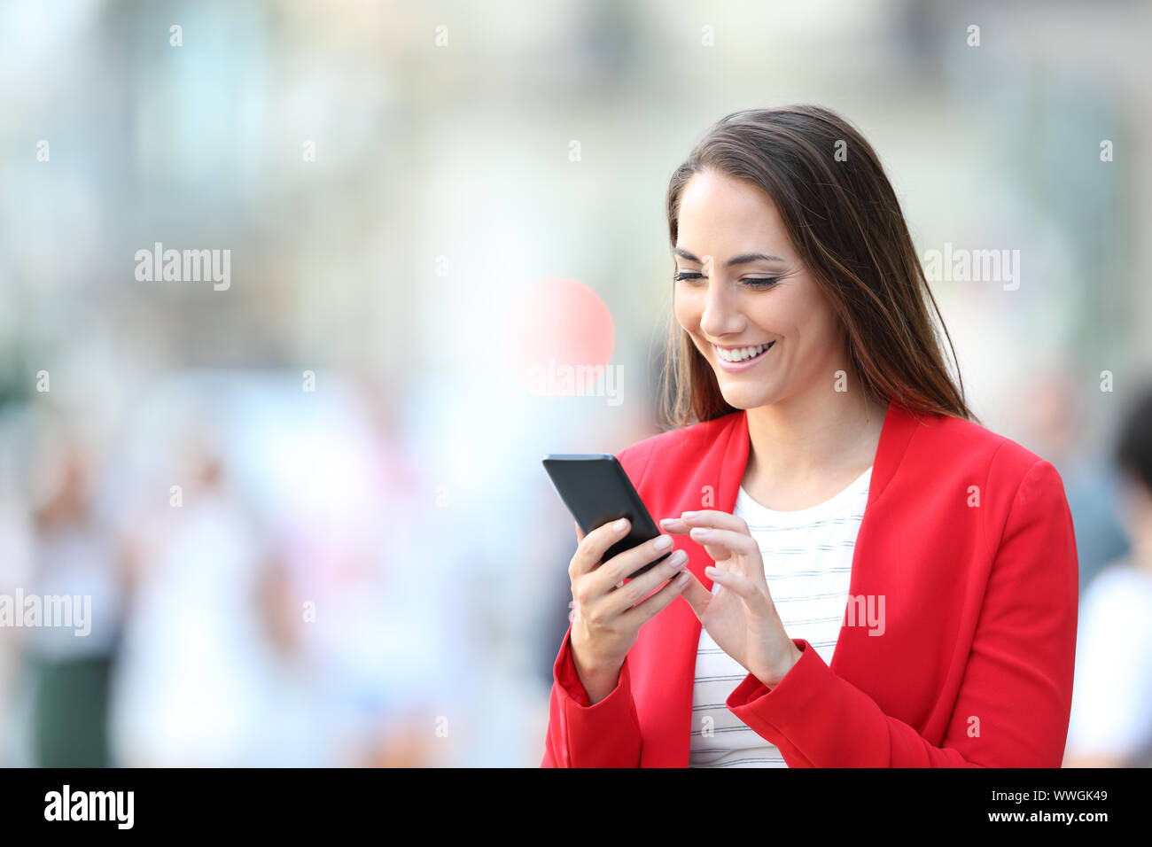 Heureux femme élégante en rouge à l'aide de smart phone debout dans la rue Banque D'Images