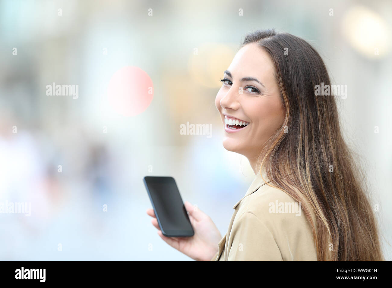 Happy woman holding smart phone ressemble au comité permanent de l'appareil photo dans la rue Banque D'Images