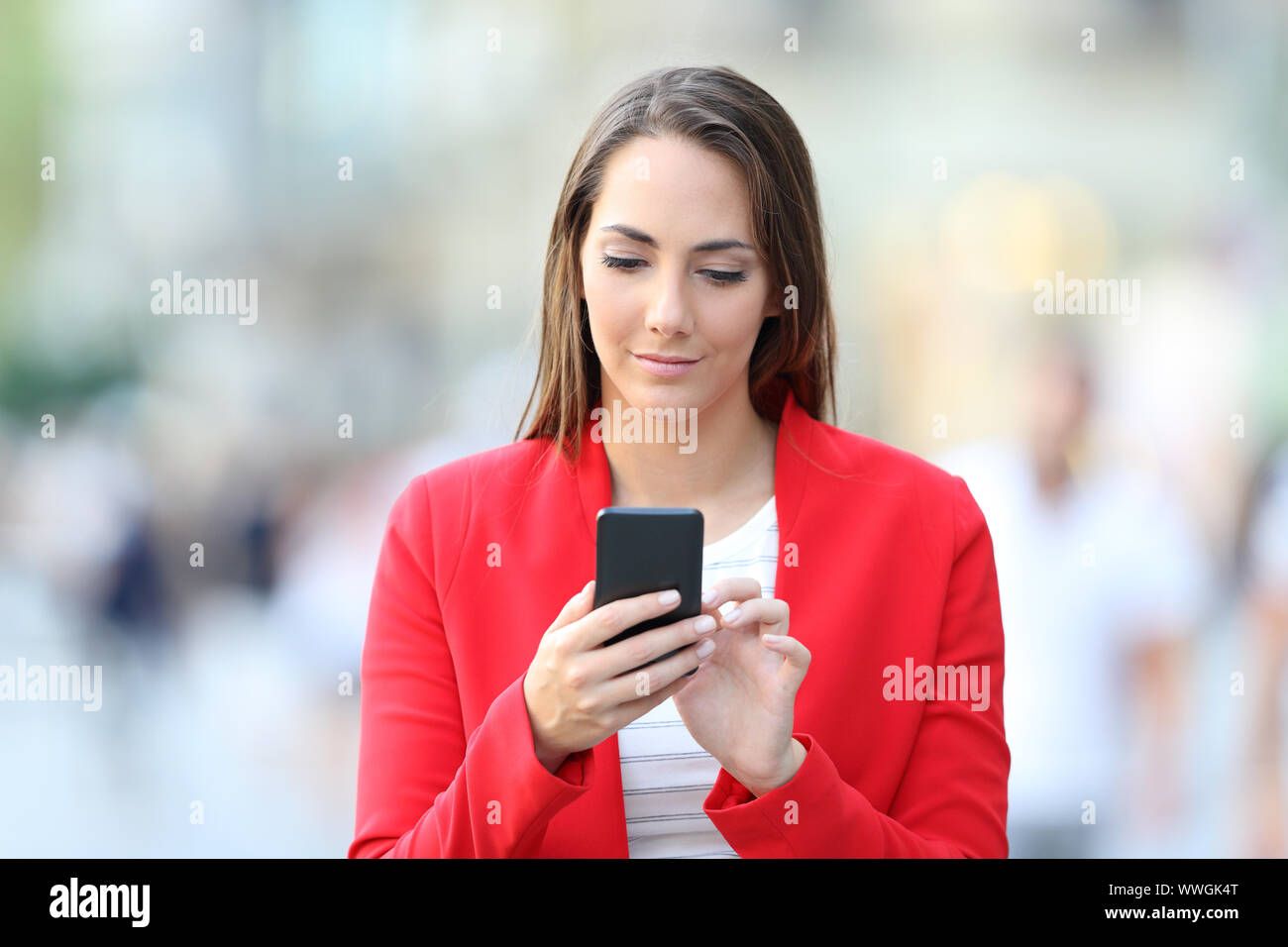 Vue avant du serious woman en rouge à l'aide de smart phone marche dans la rue Banque D'Images