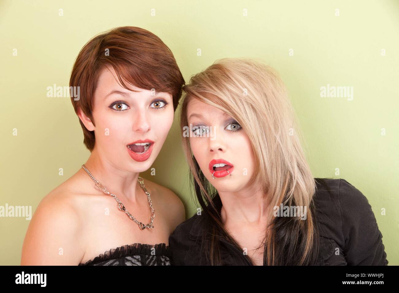 Deux jeunes filles à la punky avec expressions surpris posent devant un mur vert. Banque D'Images