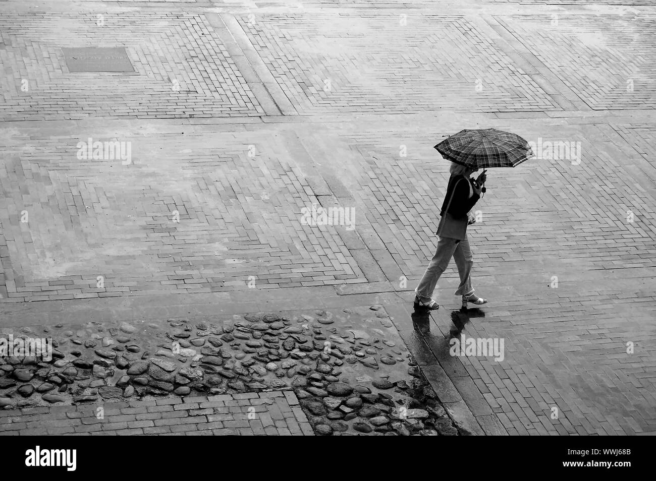 Femme avec parapluie marchant à travers la place des pluies Banque D'Images