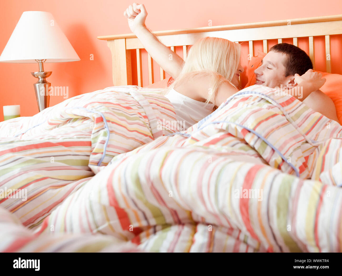 Jeune couple service et embrasser au lit sous un couvre-lit à rayures. Plan horizontal. Banque D'Images