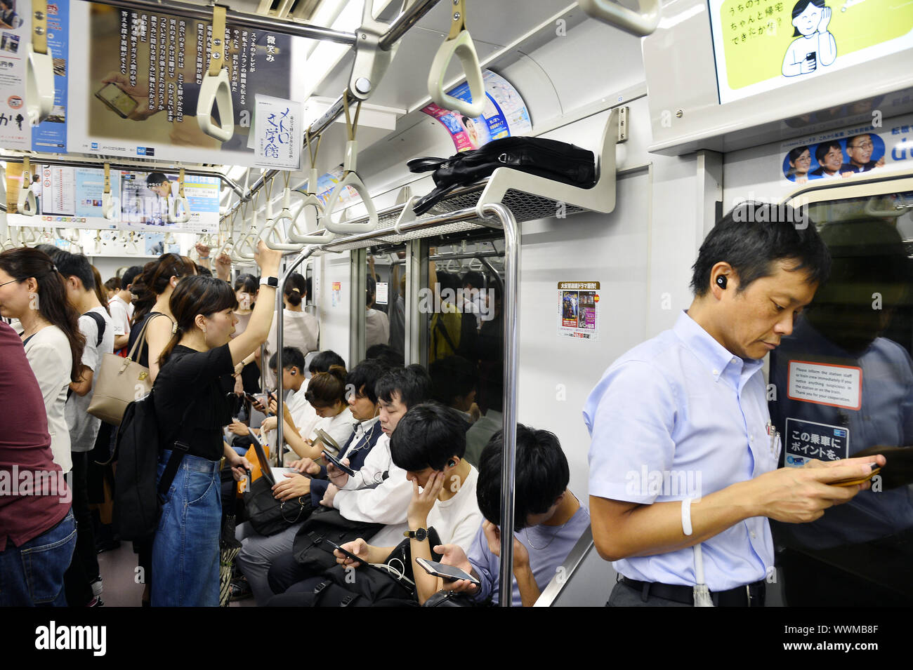 un wagon de train de banlieue bondé au Japon, où plusieurs passagers sont assis et debout tout en regardant leurs smartphones - Tokyo - Japon Banque D'Images