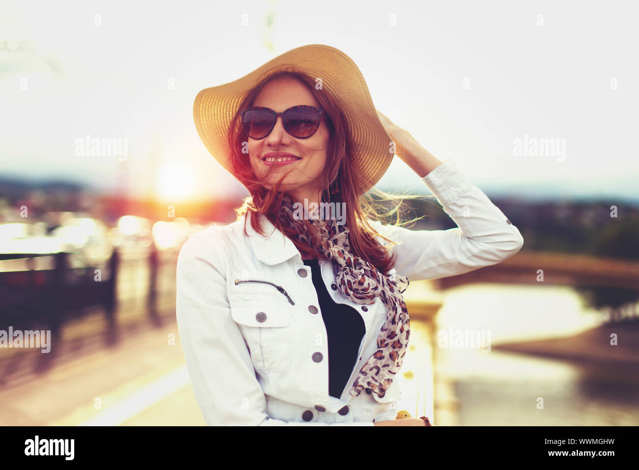 Happy young woman in hat branché à la voiture dans le coucher du soleil Banque D'Images