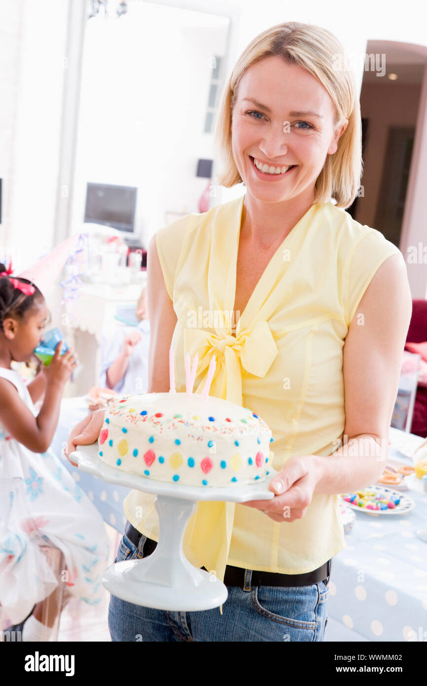 Woman at party holding birthday cake smiling Banque D'Images