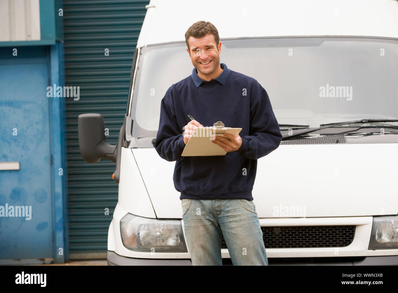 Deliveryperson standing avec van écrit dans Clipboard smiling Banque D'Images