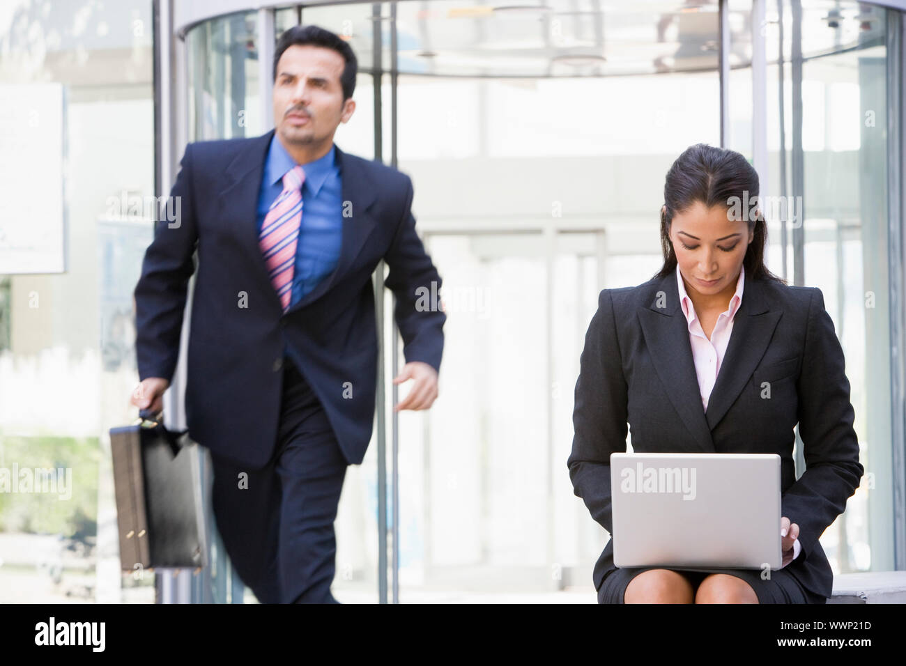 Businesswoman outdoors en face du bâtiment à l'aide d'ordinateur portable avec le businessman en arrière-plan (touche haut/flou) Banque D'Images