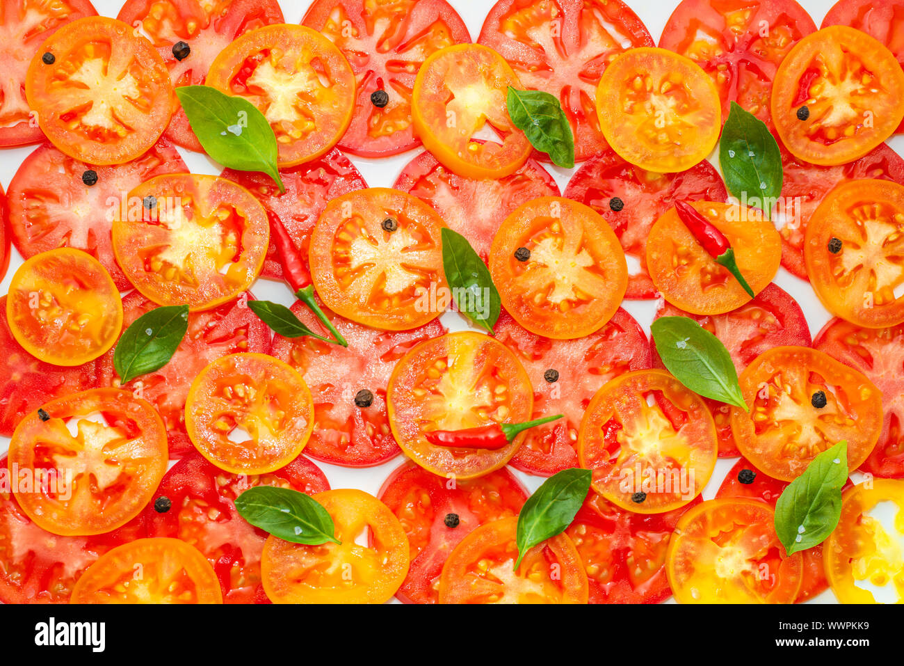 Modèle très tendance de tranches de fruits rouges, jaunes et orange décoré de tomates feuilles de basilic vert et noir, poivrons rouges sur fond blanc, télévision lay Banque D'Images