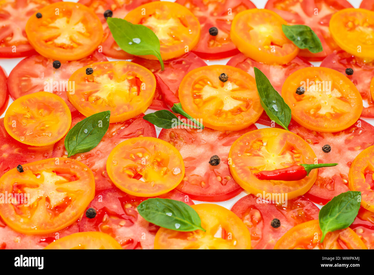 Tranches fines de fruits rouges, jaunes et orange décoré de tomates feuilles de basilic vert et noir, poivrons rouges sur fond blanc Banque D'Images