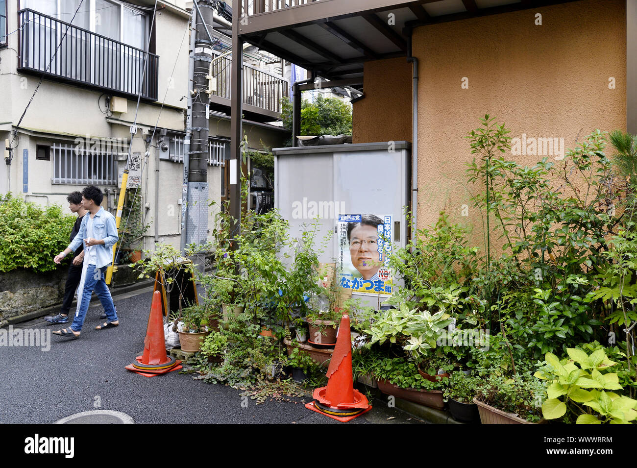 une rue résidentielle japonaise étroite avec des piétons, des plantes en pot et une affiche de campagne politique fixée à une armoire extérieure de service/stockage Banque D'Images