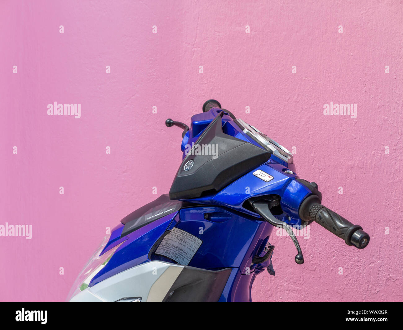 Le sommet d'un scooter montrant un guidon et cowling bleu contre un mur rose Banque D'Images