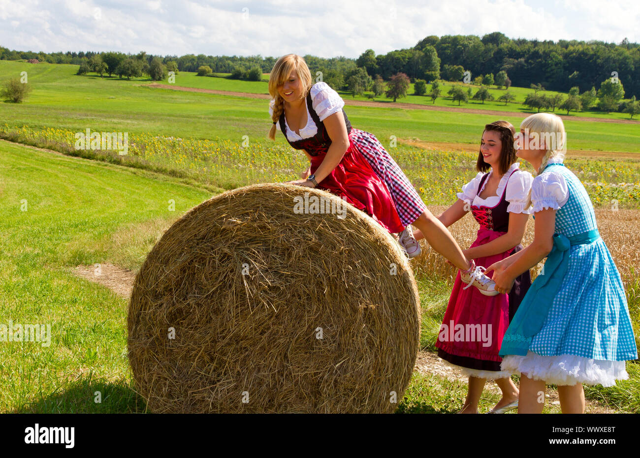 Trois cheerful in dirndl sur un champ avec une botte de paille Banque D'Images