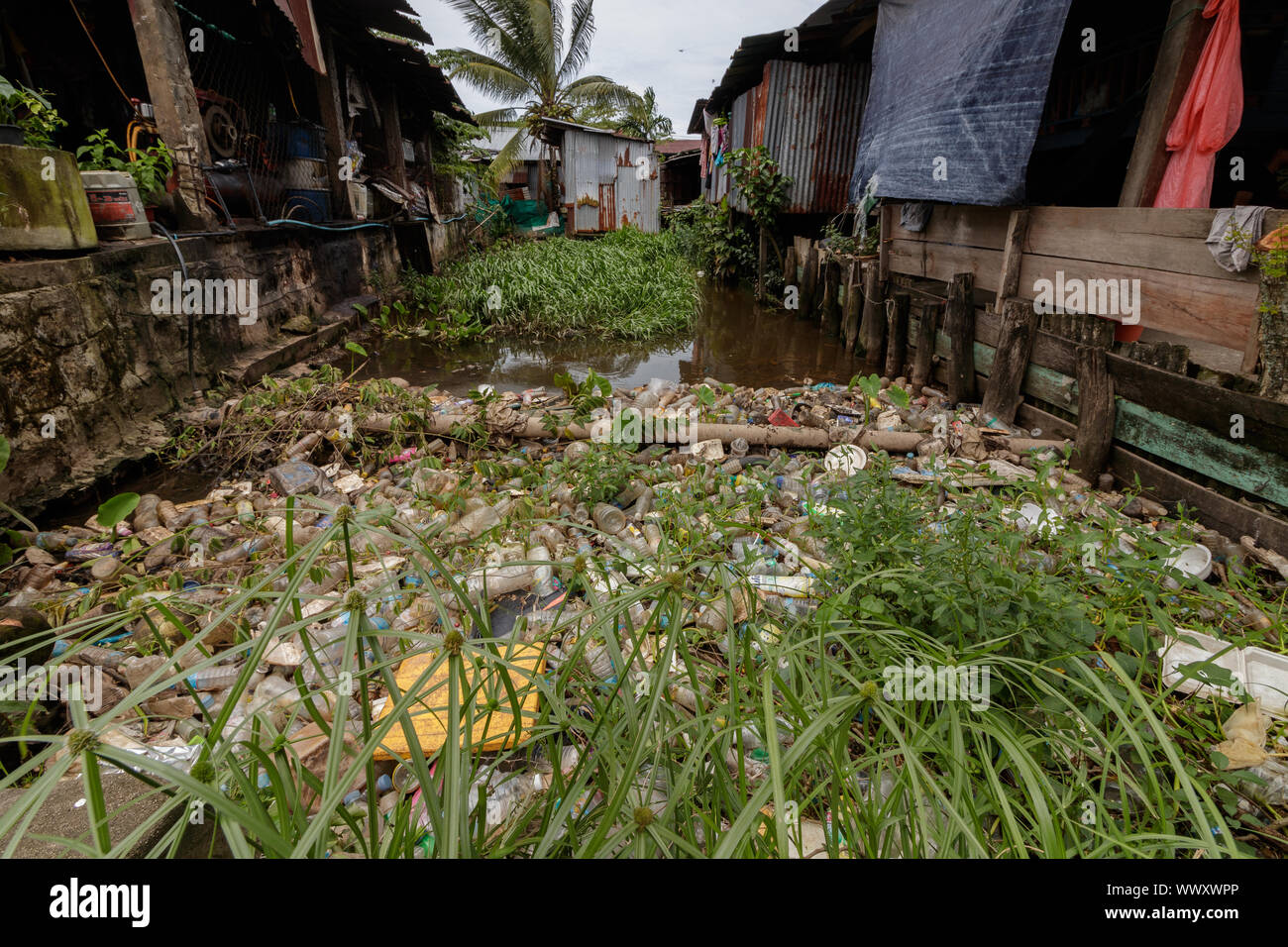 Une rivière qui coule entre les maisons bidonvilles au Cambodge remplis de déchets plastiques. Banque D'Images