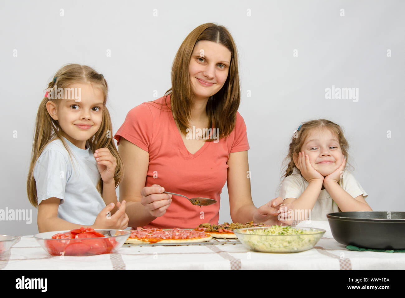 Mère de deux petites filles assise à la table de la cuisine préparer une pizza Banque D'Images