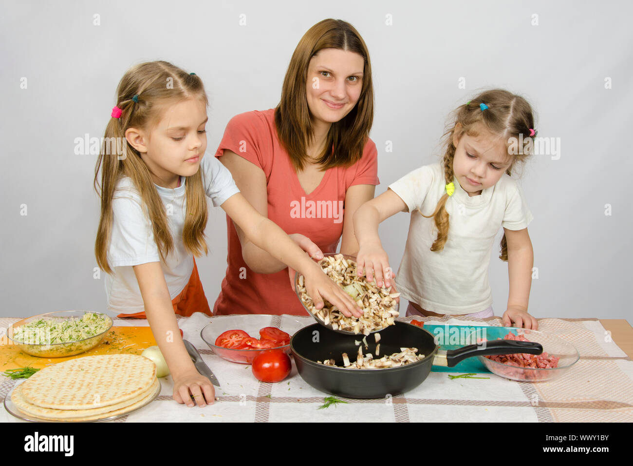 Deux petites filles à la table de la cuisine avec un zèle à aider sa mère pour les champignons de la plaque à la casserole Banque D'Images