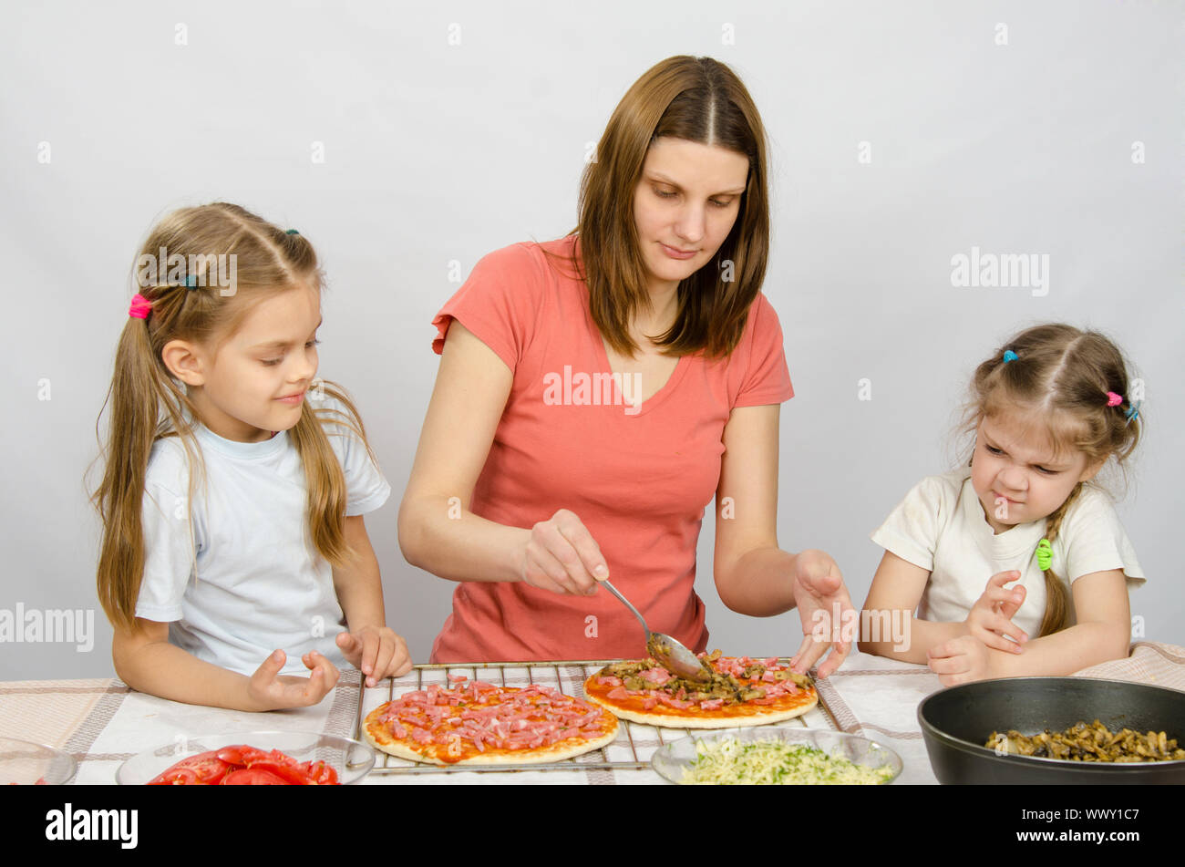 Deux petites filles assise à la table de la cuisine et de regarder en tant que mère de préparer une pizza Banque D'Images