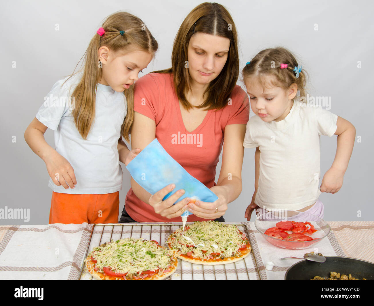Deux petites filles observent avec intérêt que la mère est d'arroser la mayonnaise pizza Banque D'Images