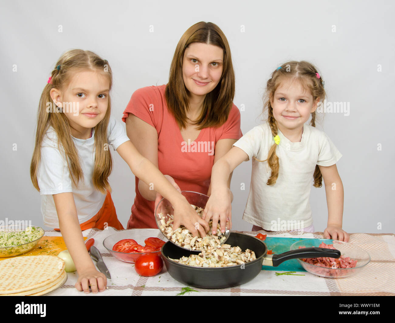 Deux petite fille à la table de la cuisine pour aider sa mère champignons hachés de la plaque à la casserole Banque D'Images