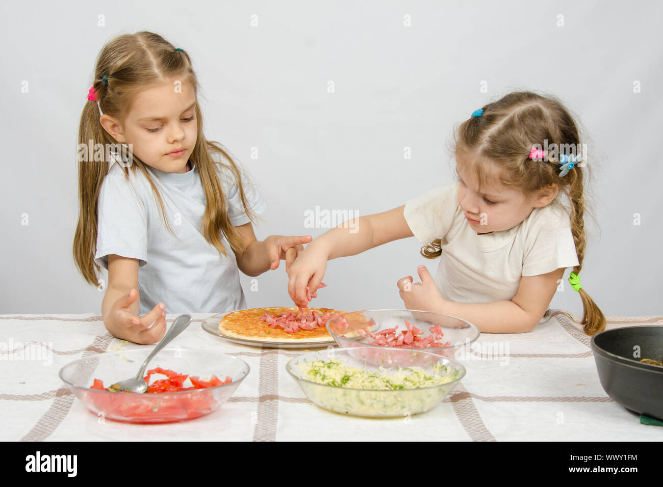 Fille de six ans, observe et contrôle sa jeune sœur met sur la pizza ingrédients Banque D'Images