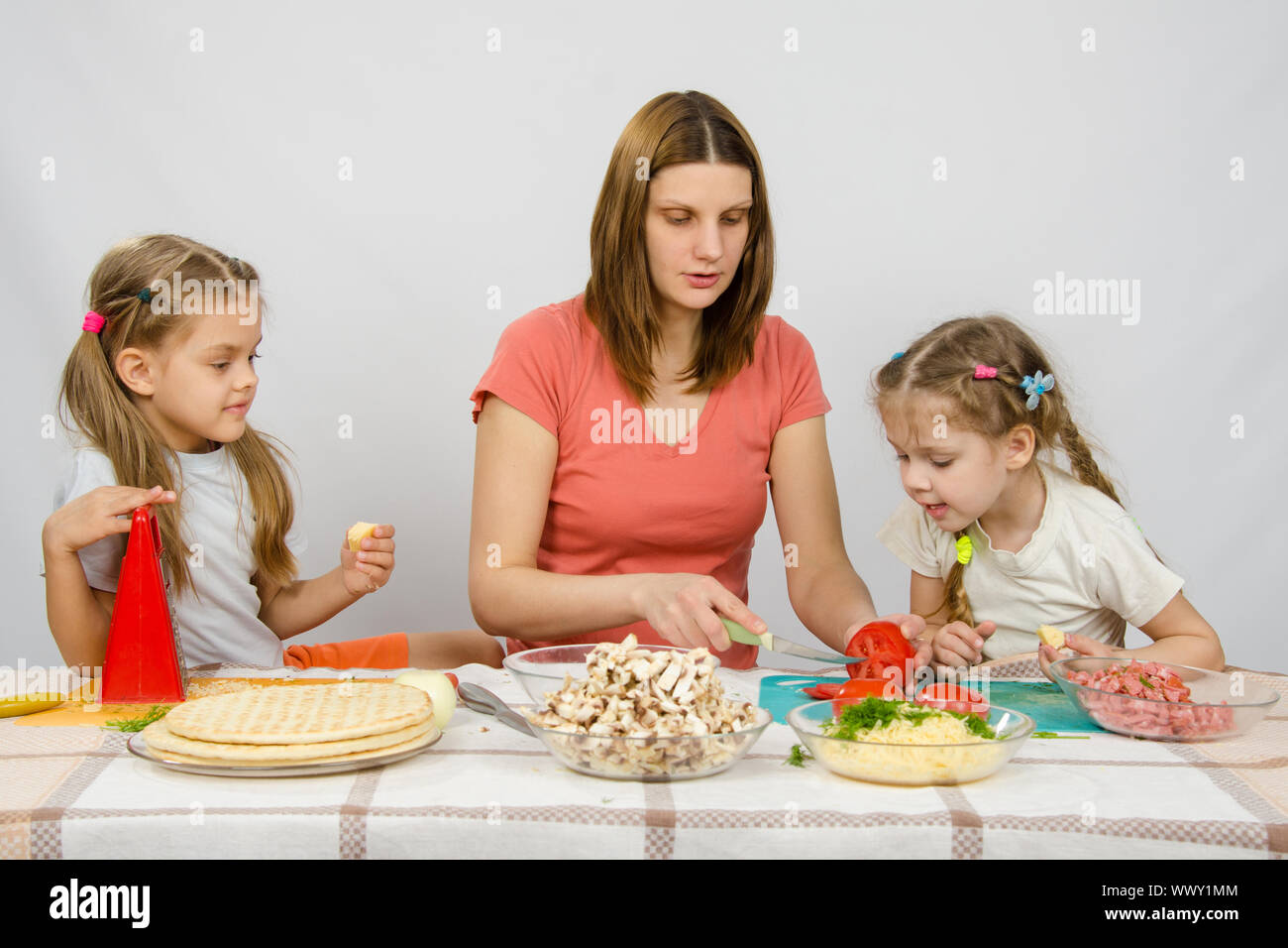 Maman montre deux jeunes filles à la table de cuisine comme la coupe tomato pizza Banque D'Images