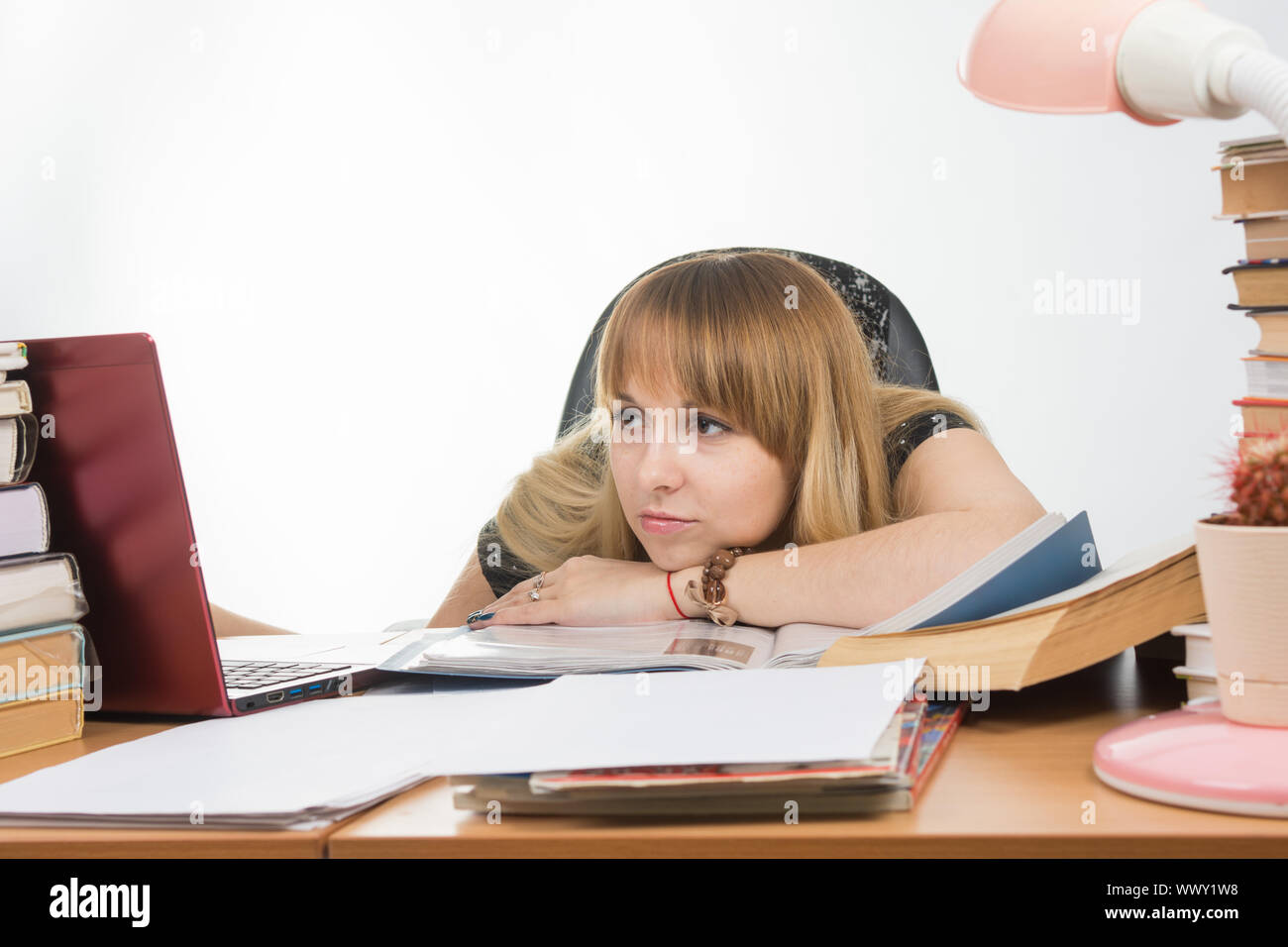 La jeune fille à la réception encombrée de livres et papiers malheureusement regarde le portable avec sa tête reposant sur sa main sur la table Banque D'Images