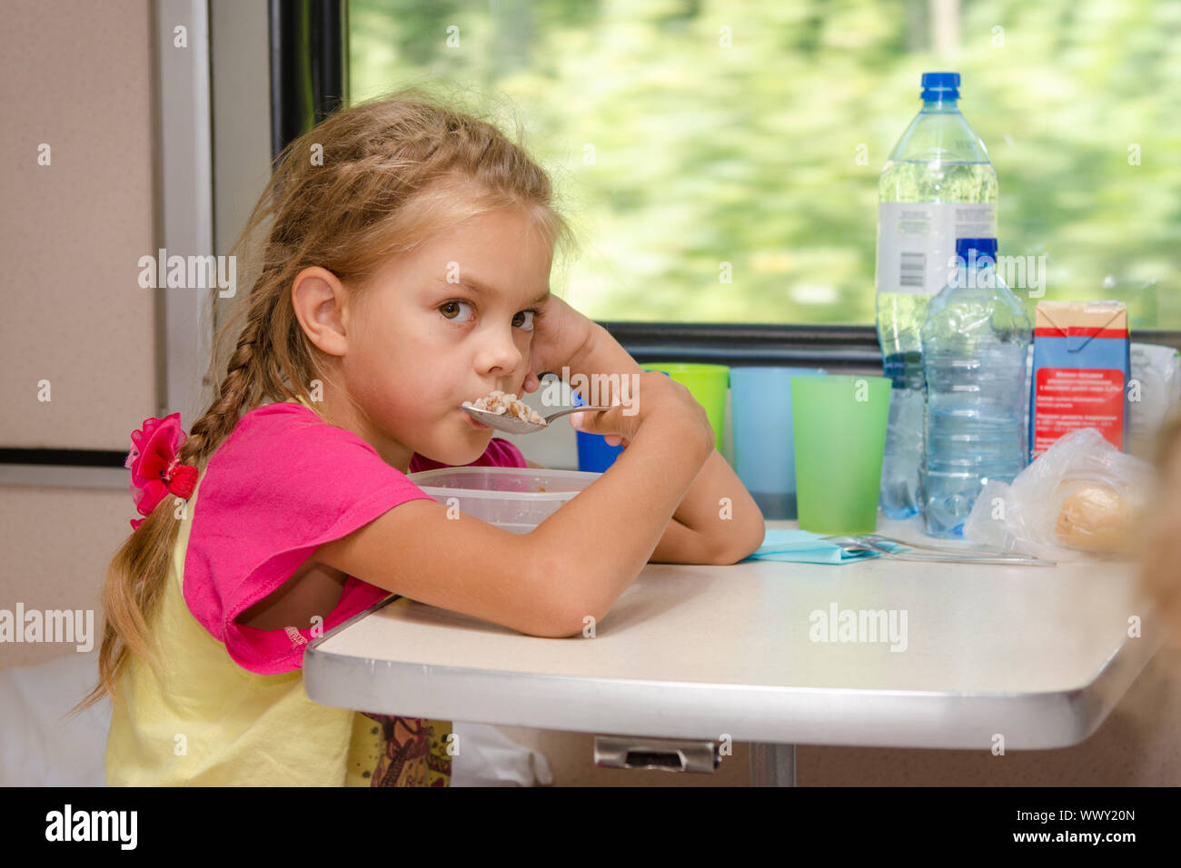 Une fille de six ans dans un train assis à la table sur la place inférieure dans le compartiment de deuxième classe de la voiture et mange du gruau Banque D'Images