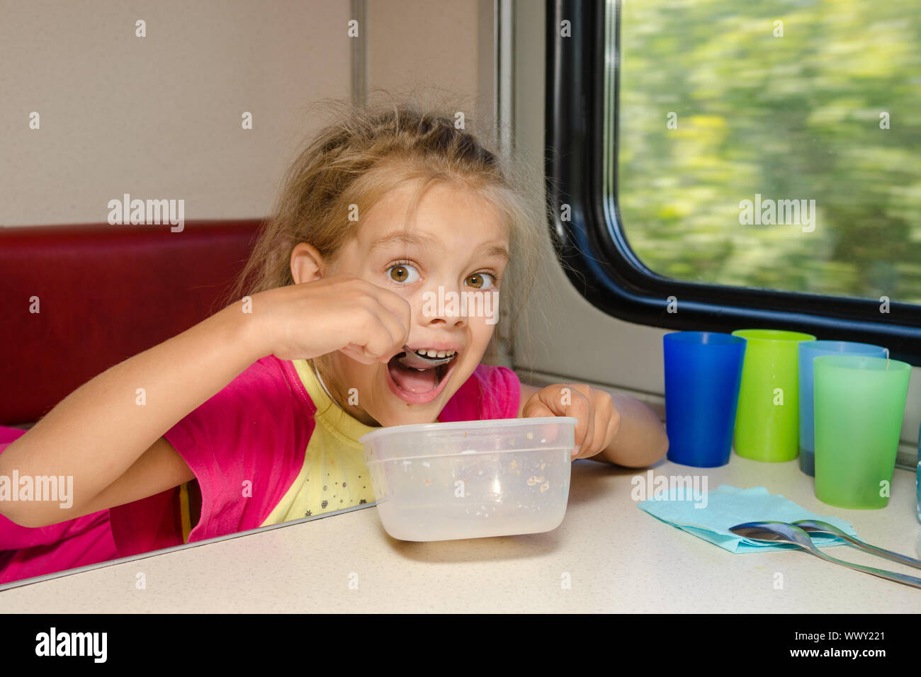 La jeune fille dans le train est assis à une table sur la place inférieure dans le compartiment de deuxième classe de la voiture et le mange avec délectation spoo Banque D'Images