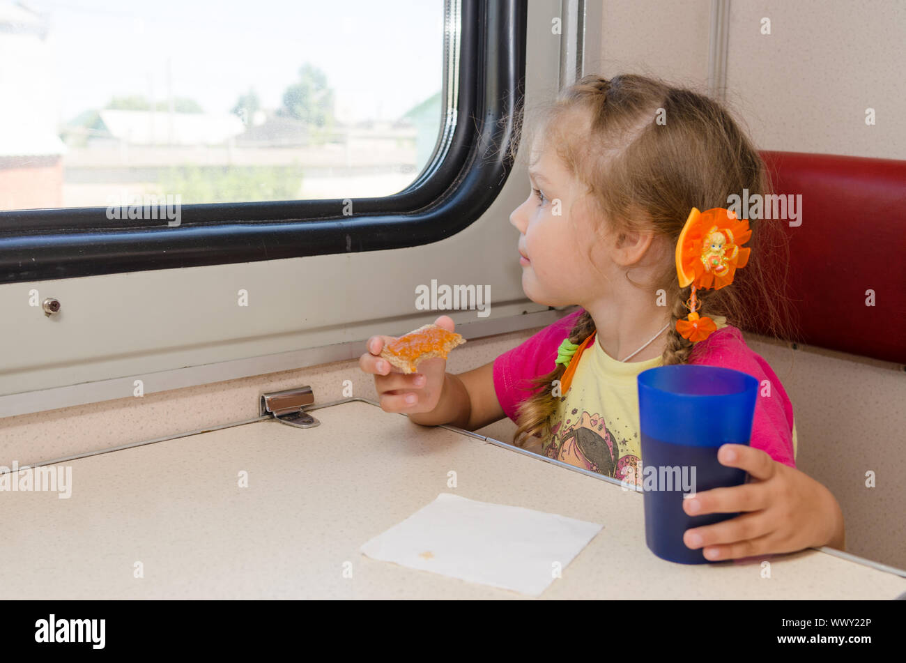 Petite fille de boire le thé avec un sandwich dans le train à la table sur l'extérieur du chariot de deuxième classe et avec enthousiasme lookin Banque D'Images