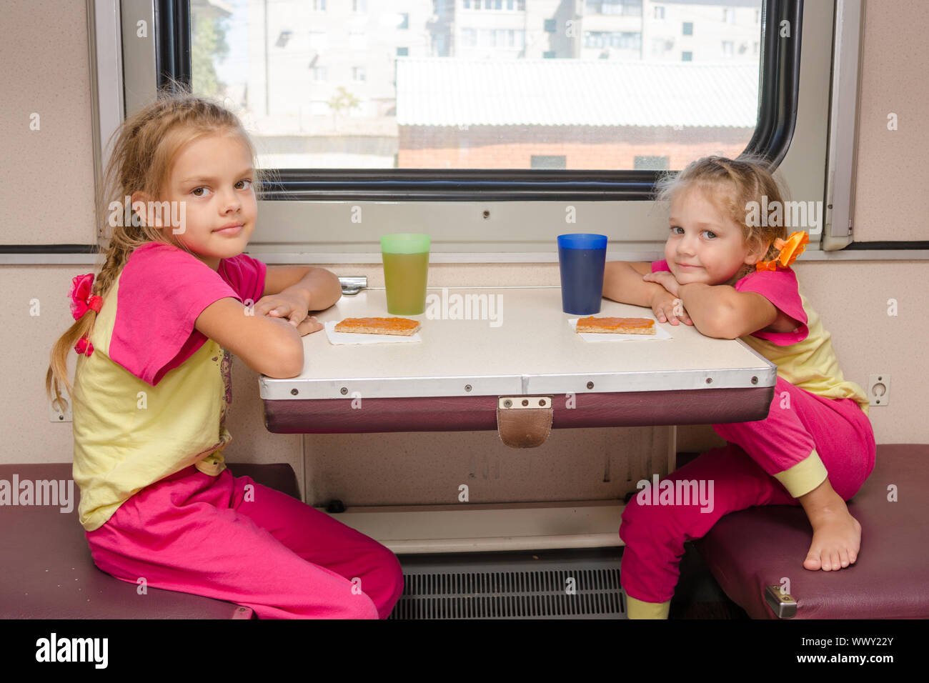 Deux petites filles dans le train assis à la table de la voiture de seconde classe hors-bord dans les mêmes vêtements Banque D'Images