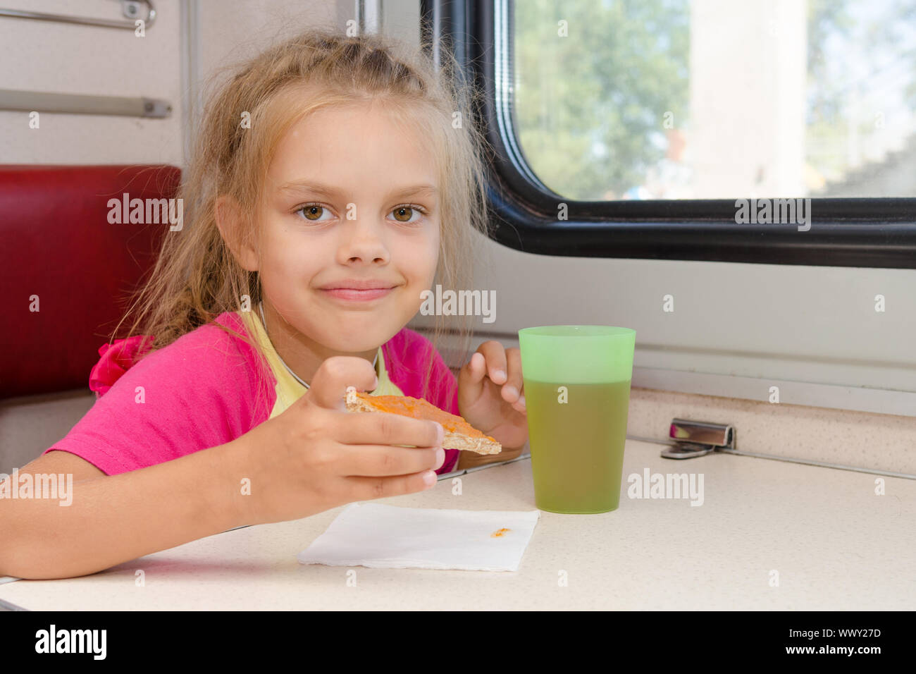 Fille de six ans de boire le thé avec un sandwich dans le train à la table sur le transport de deuxième classe hors-bord Banque D'Images