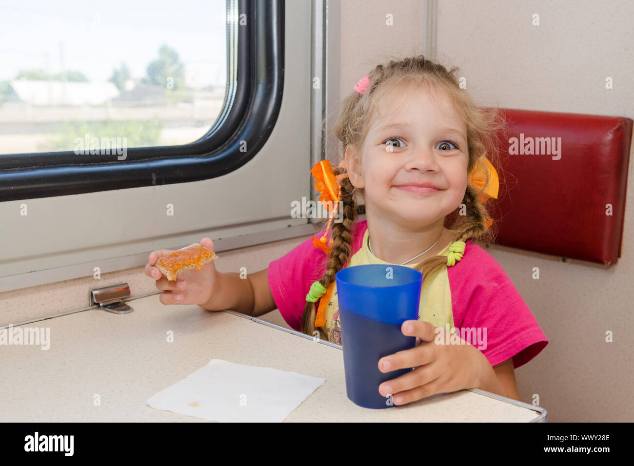 Petite fille avec un visage heureux boire du thé avec un sandwich dans le train à la table sur le transport de deuxième classe hors-bord Banque D'Images