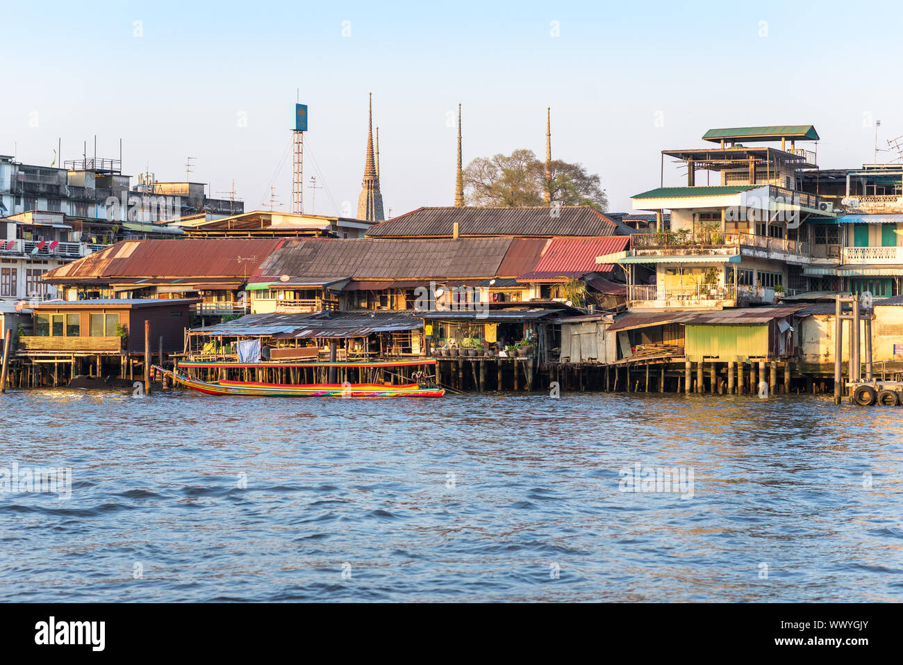 Bateau à longue queue en face de maisons sur pilotis le long de la rivière Chao Phraya à Bangkok Banque D'Images