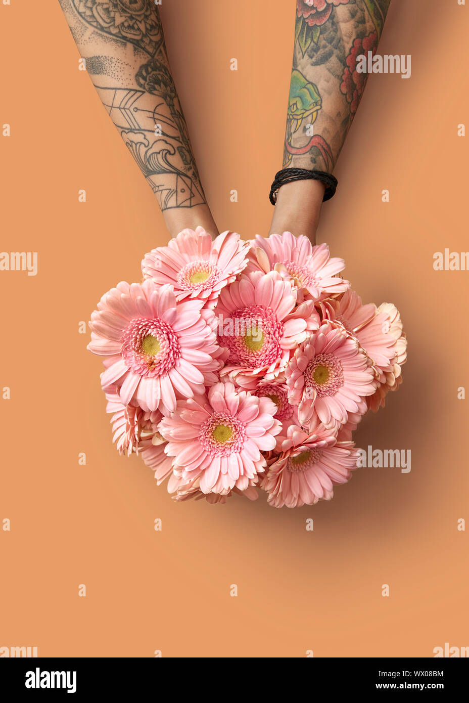 Mains d'une femme avec un tatouage tenir un beau bouquet avec gerberas rose sur fond orange Banque D'Images