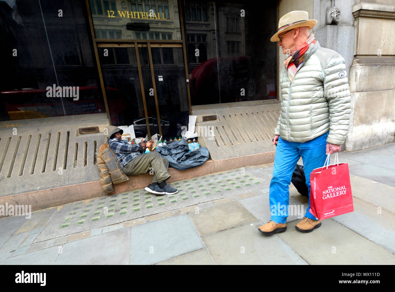 Londres, Angleterre, Royaume-Uni. L'homme avec un sac de la National Gallery en passant devant un sans-abri dans la région de Whitehall Banque D'Images