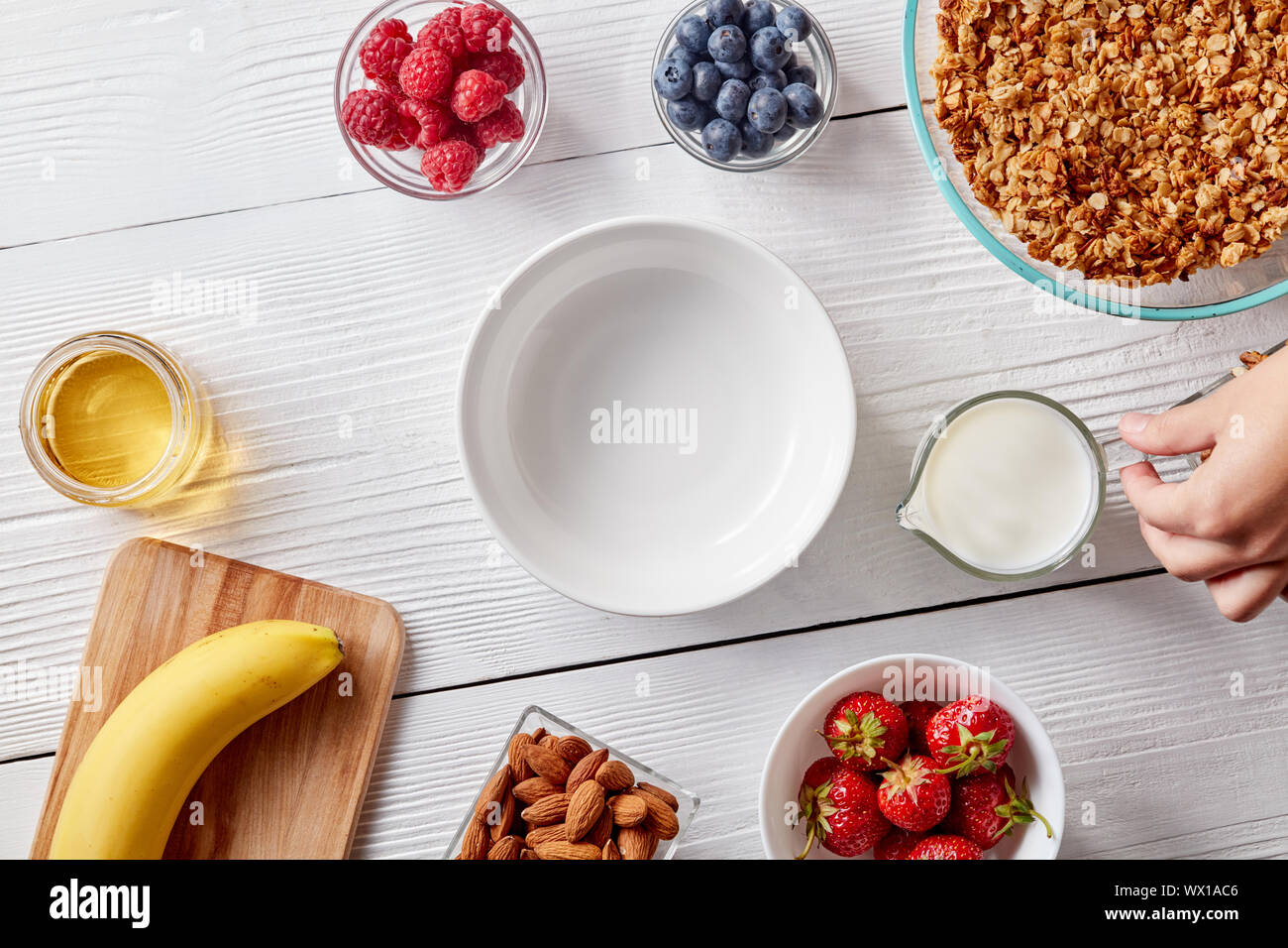 Les baies mûres, granola, noix, miel et une plaque vide sur une table en bois blanc. A woman's hand est titulaire d'un verre de lait. Dietary foo Banque D'Images