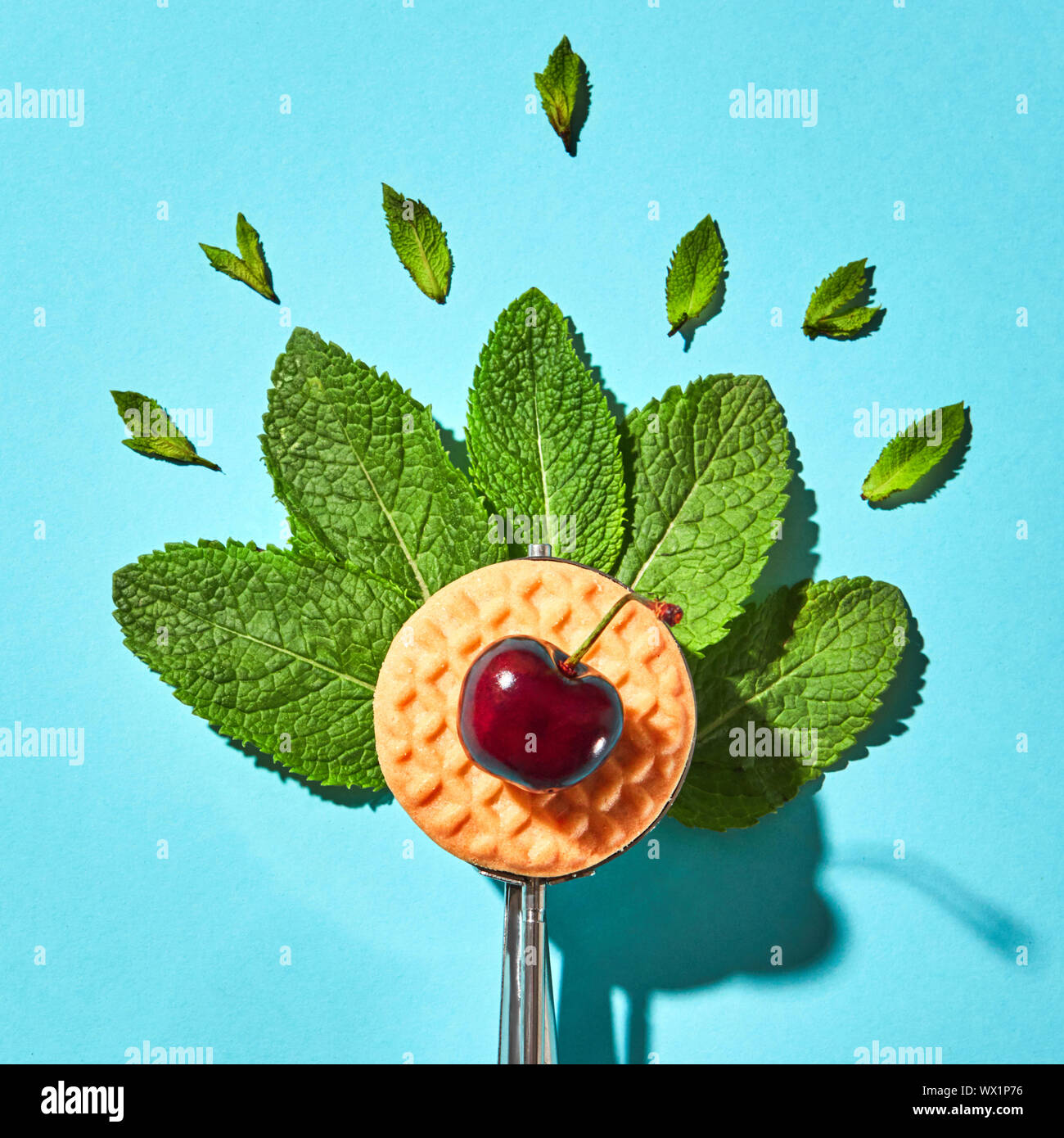 Mise à plat d'une cuillère de crème glacée avec des feuilles de menthe, biscuit et cerise sur un fond bleu avec des ombres. Concept alimentaire. Banque D'Images